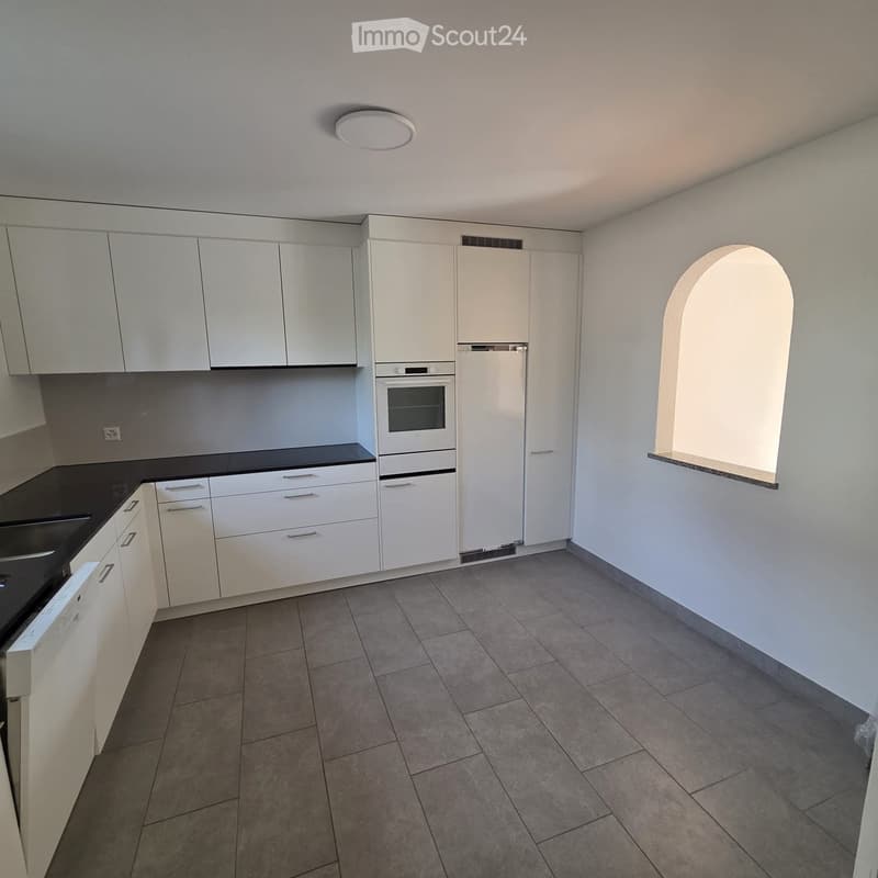 Modern kitchen with white cabinets, black countertops, tiled floor, and built-in appliances including a refrigerator, oven, and dishwasher.