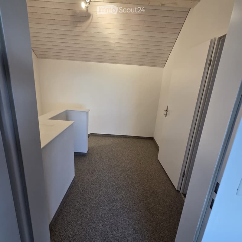 Empty hallway with grey carpeted floor, white walls, and a small white bench on the left side.
