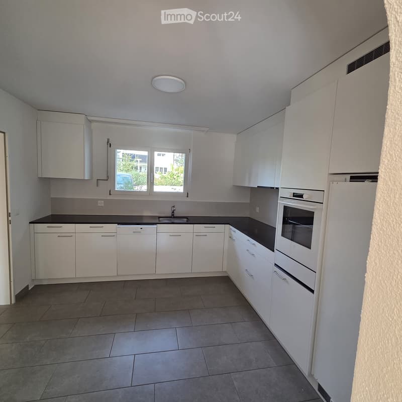 Modern kitchen with white cabinets, black countertops, and built-in appliances including a refrigerator, oven, and dishwasher. The space features a window with a view of greenery outside.