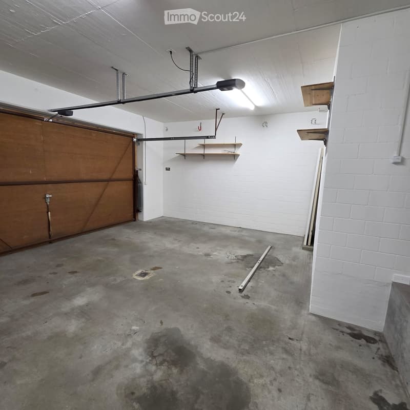 Empty garage with concrete floor, white brick walls, wooden door, and shelves.