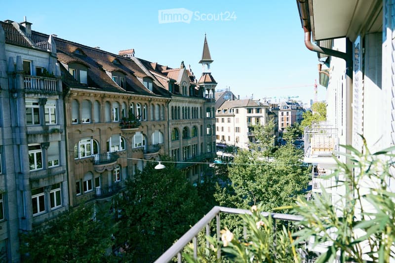 Balcony overlooking a cityscape with historic buildings, trees, and a clear blue sky.