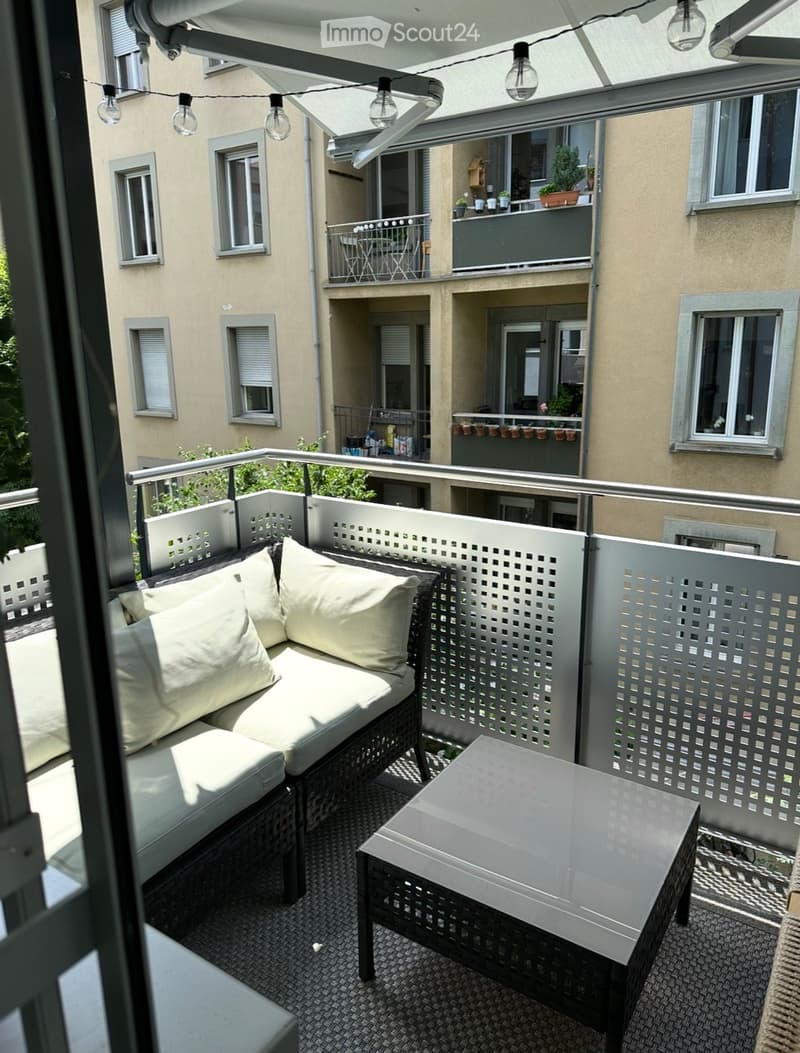Balcony with a white cushioned sofa, a small table, and decorative lattice fencing. The balcony is part of a multi-story residential building with visible neighboring balconies and windows.