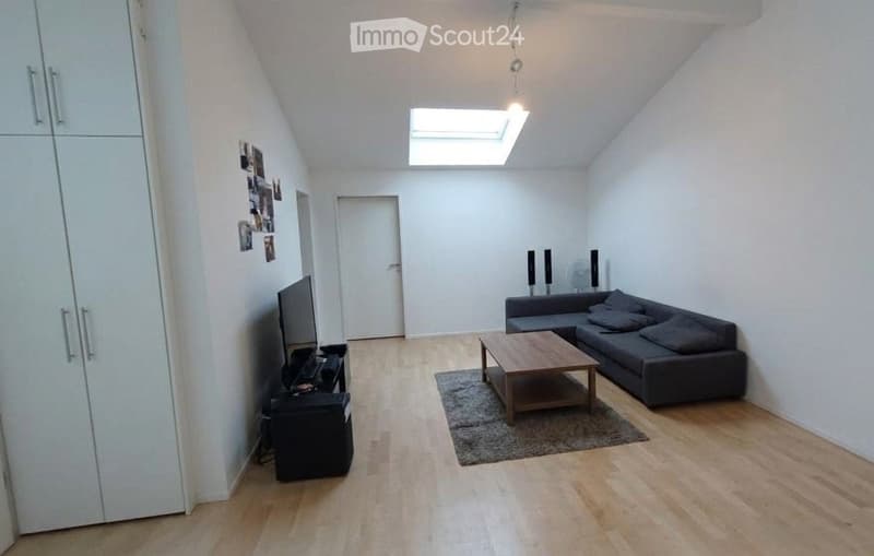 Modern living room with wooden flooring, grey sectional sofa, coffee table, TV, and a large skylight providing natural light.