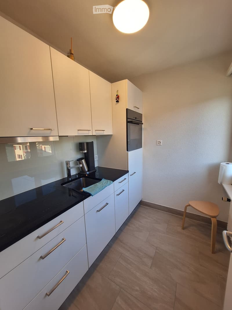 Modern kitchen with white cabinets, black countertops, stainless steel appliances, and a small wooden stool.