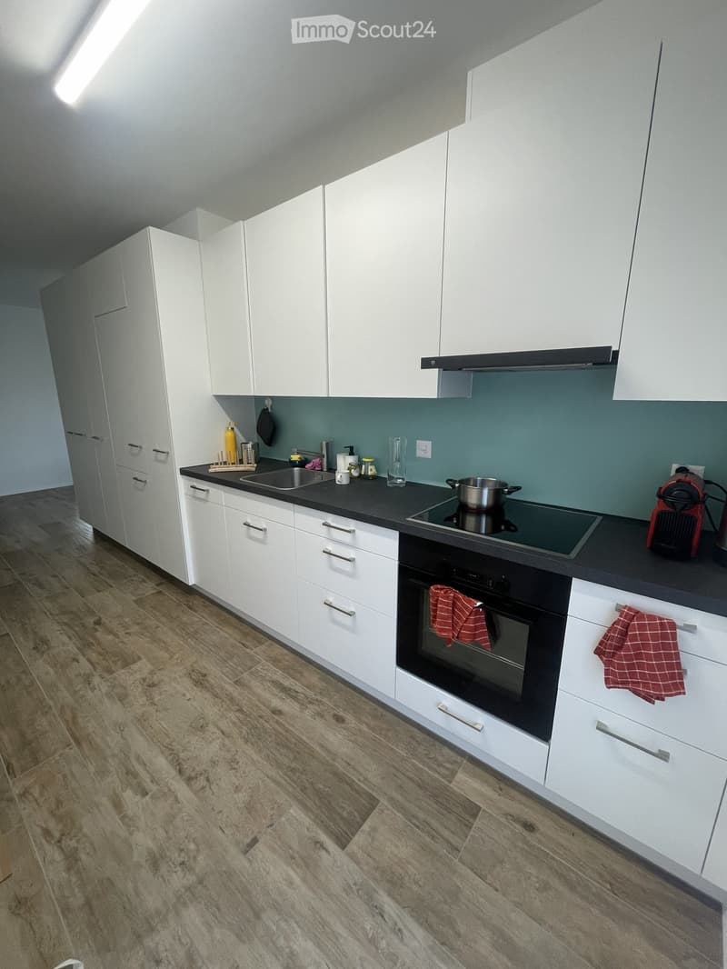 Modern kitchen with white cabinets, black countertops, and stainless steel appliances. Features include a sink, stove, oven, and various small appliances.