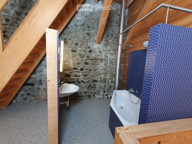 Bathroom with stone walls, wooden beams, a sink, and a bathtub with blue patterned curtains.