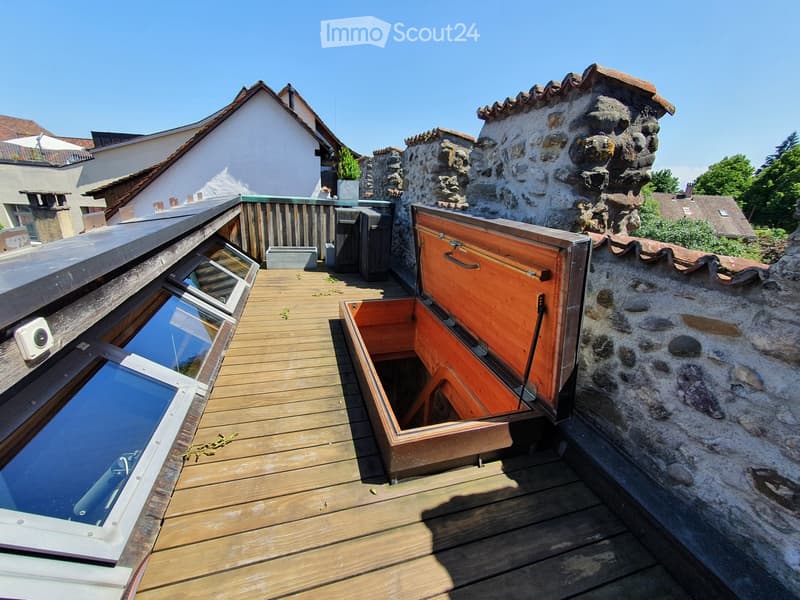 Wooden deck with open skylight hatches, stone chimney, and surrounding buildings.