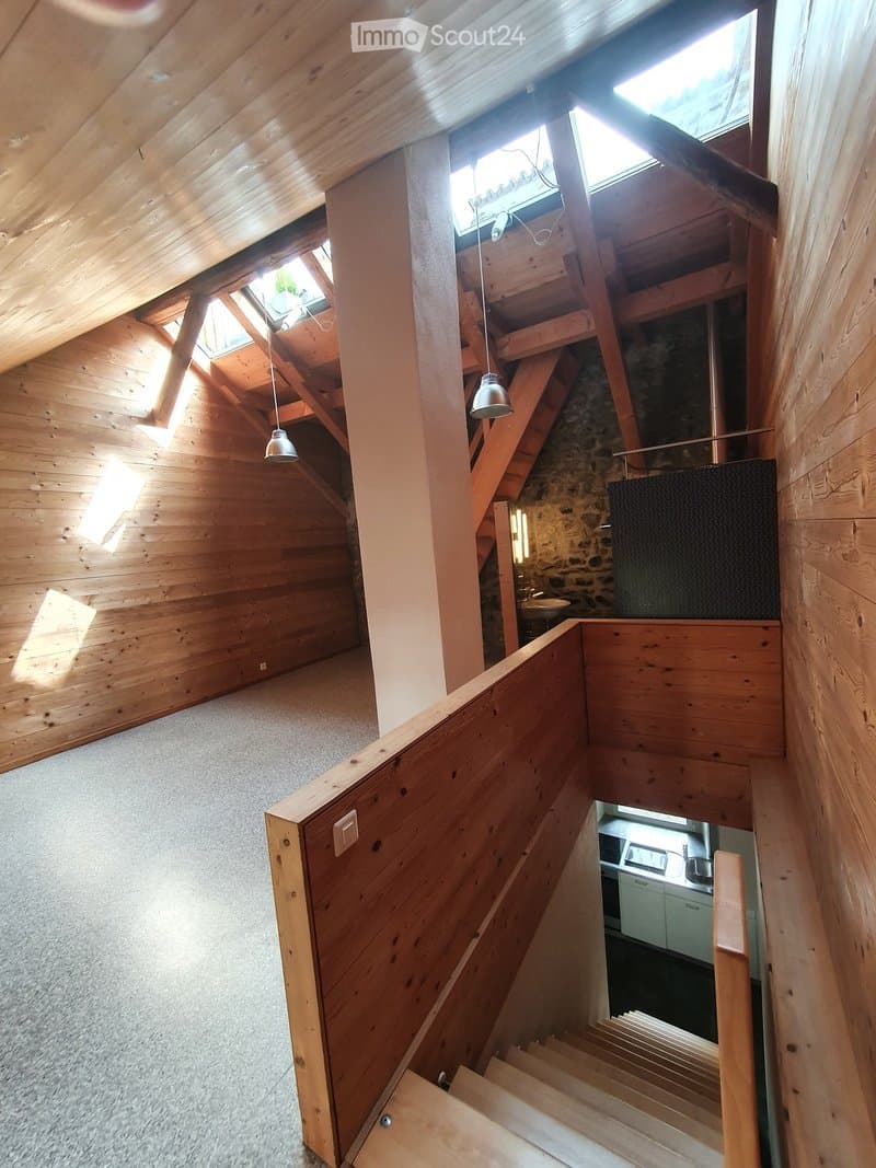 Wooden staircase with a modern design, featuring exposed wooden beams and skylights, leading to a lower level with a visible kitchen area.