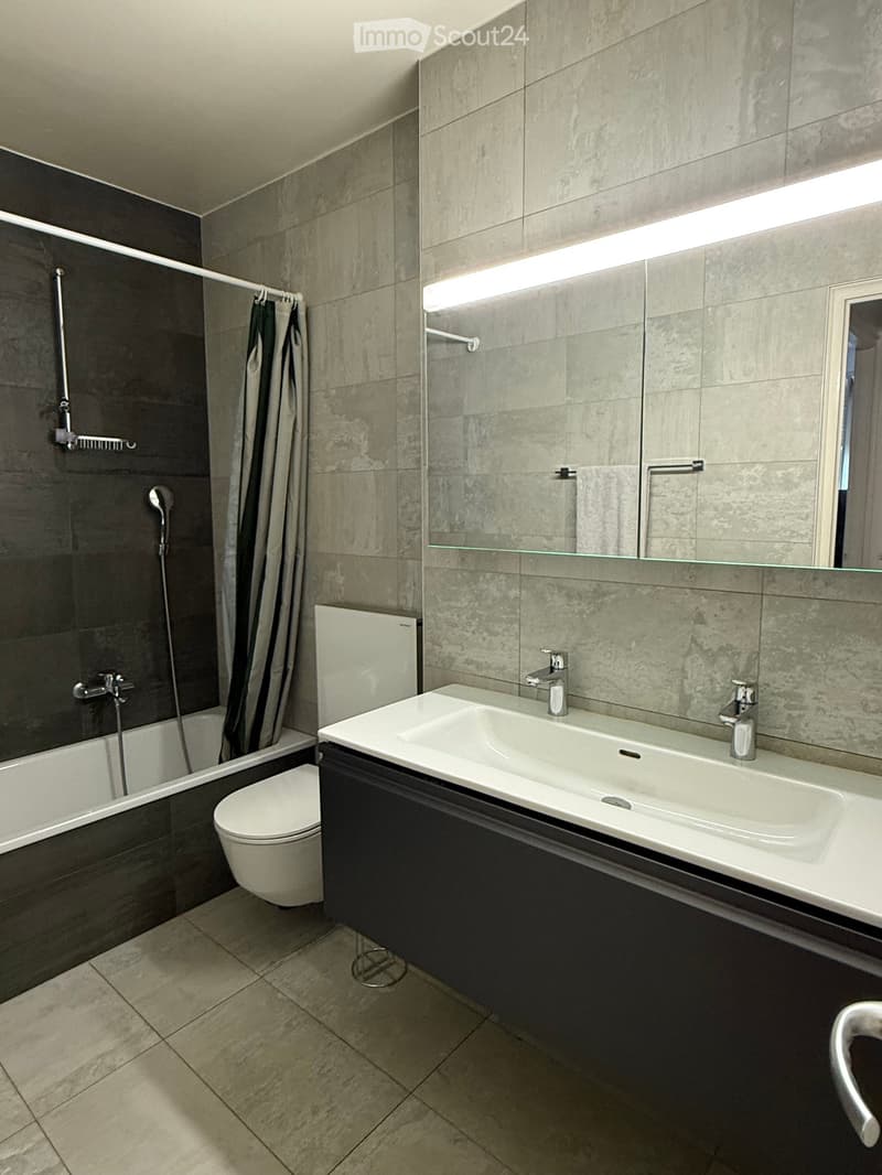 Modern bathroom with a bathtub, toilet, double sink, large mirror, and shower area with a curtain.