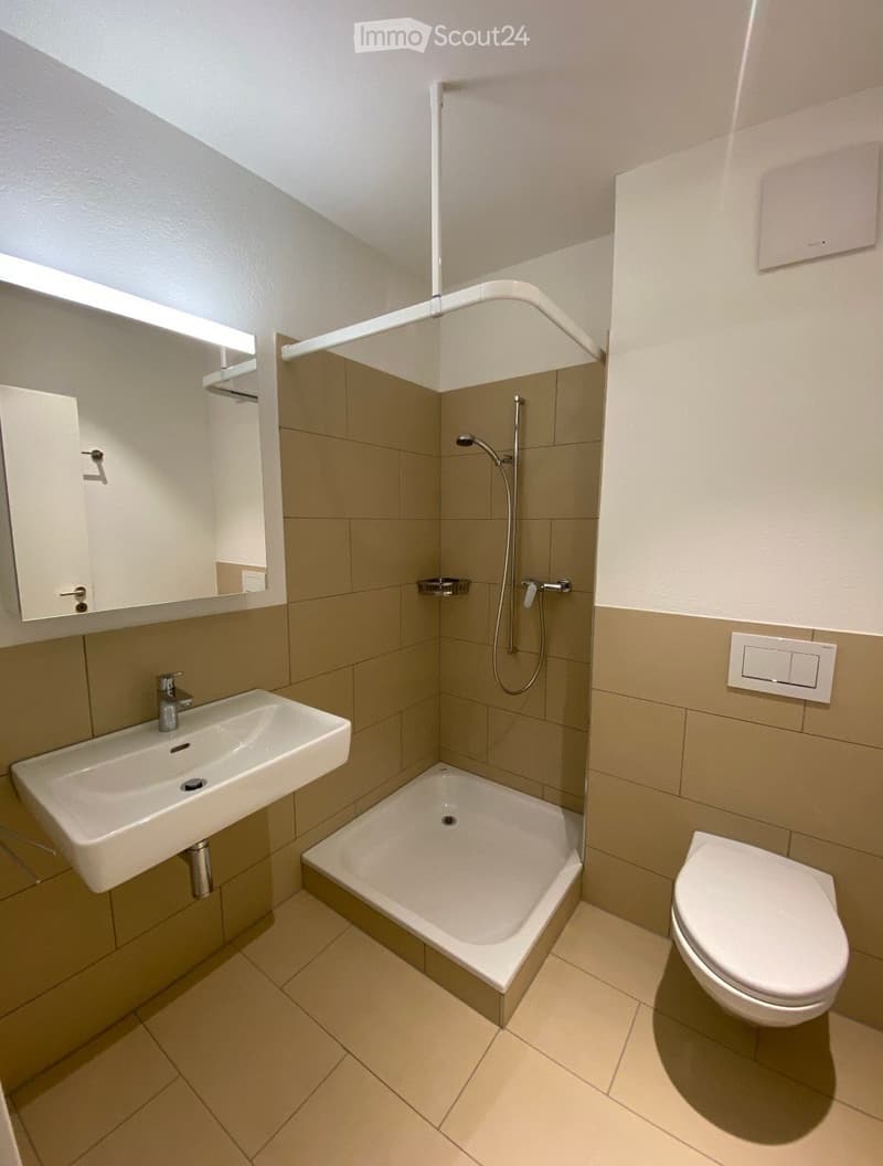 Modern bathroom with a white sink, bathtub, toilet, and mirror. Beige tiles and a sleek design.