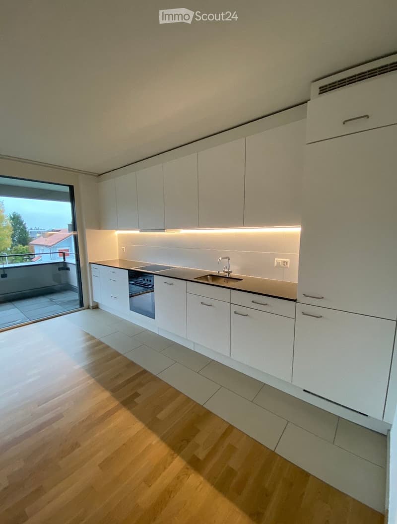 Modern kitchen with white cabinets, wooden flooring, and a large window overlooking a balcony.