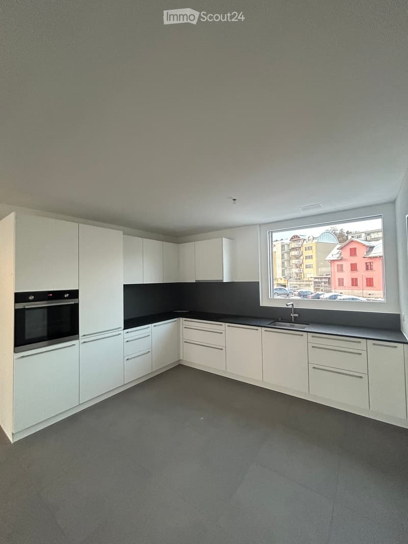 Modern kitchen with white cabinets, black countertops, and a large window overlooking a cityscape.