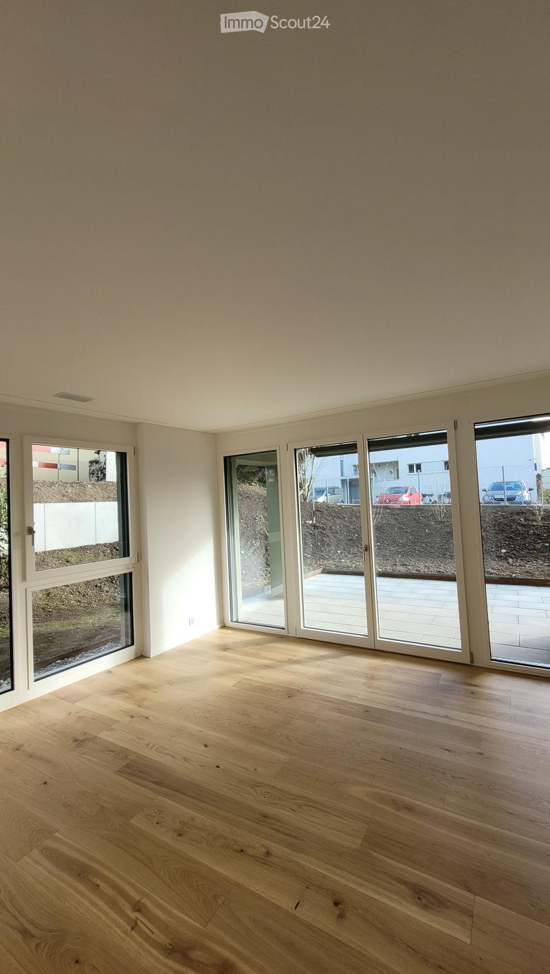Empty room with light wooden flooring, large glass sliding doors leading to an outdoor area, and white walls.