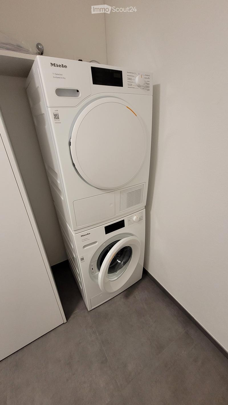 A compact bathroom with a white Miele washing machine and dryer stacked vertically, featuring a control panel and digital display.
