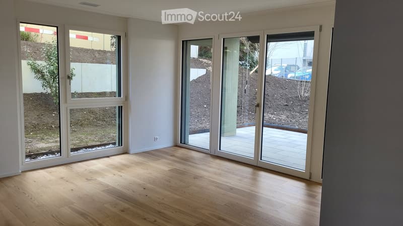 Empty room with wooden flooring, large windows, and sliding glass doors leading to an outdoor area.