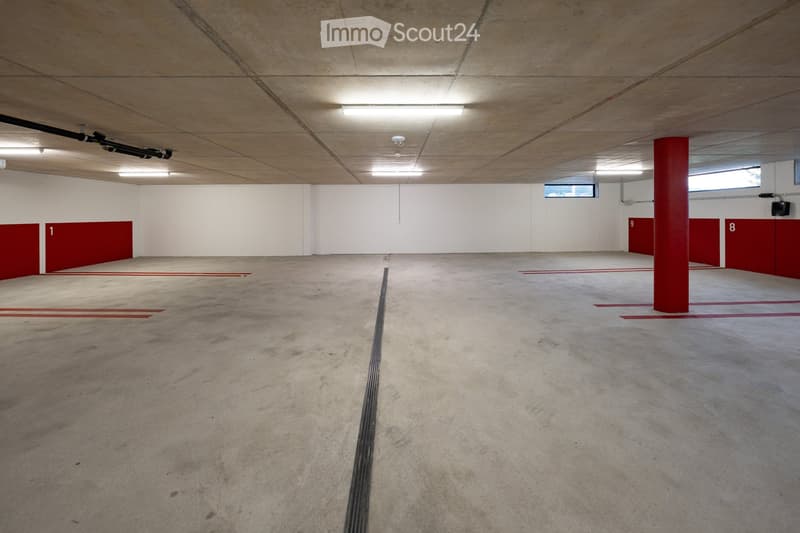 Empty underground parking area with concrete floors, white walls, red pillars, and numbered parking spots.