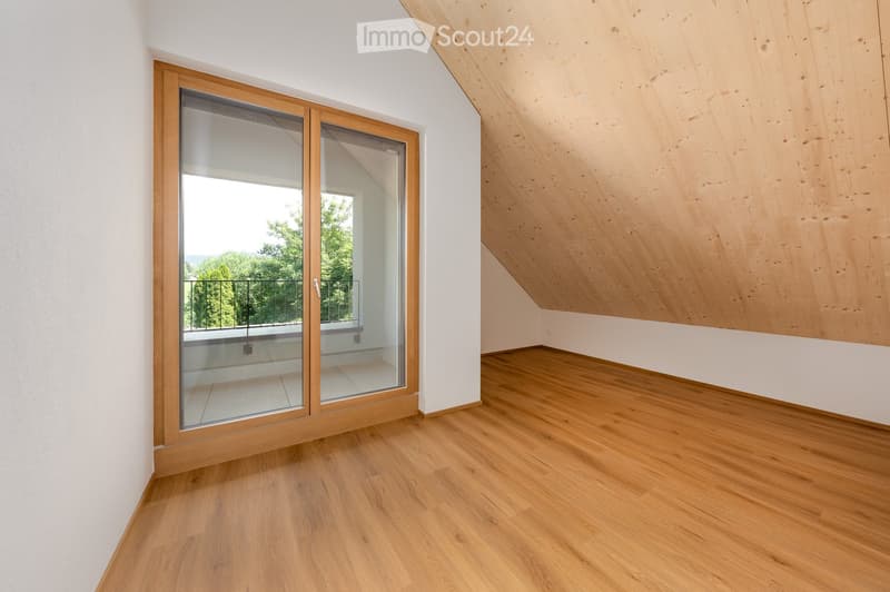 Empty room with wooden flooring, white walls, and a large sliding glass door leading to a balcony with a view of greenery.