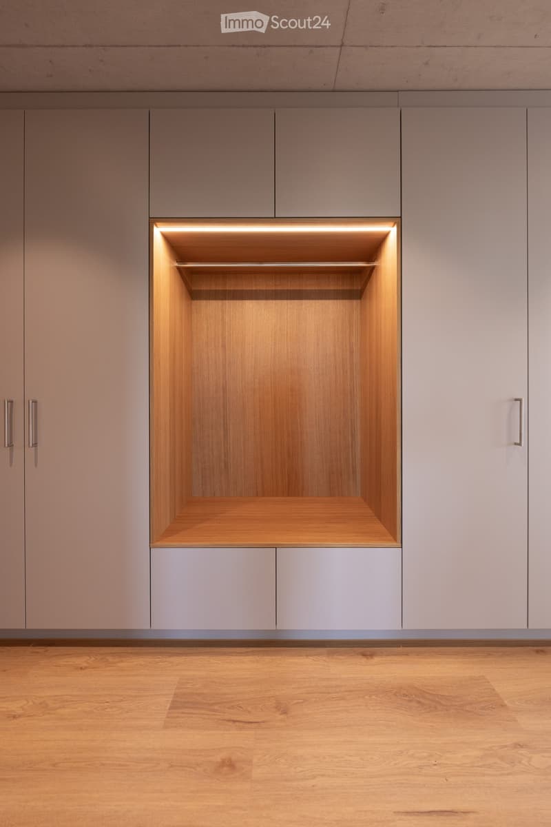 Empty room with light grey cabinets, wooden floor, and built-in shelving illuminated by soft lighting.