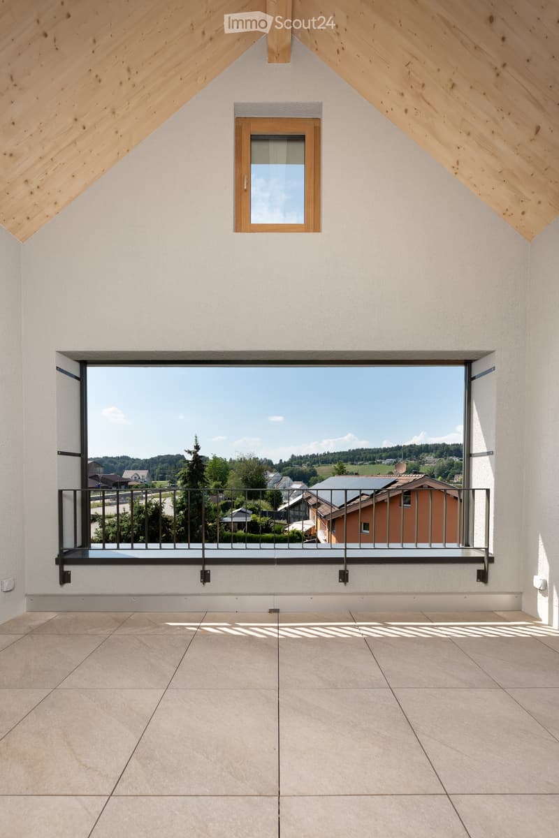 Modern balcony with large windows, metal railing, and tiled floor, overlooking a scenic countryside view.