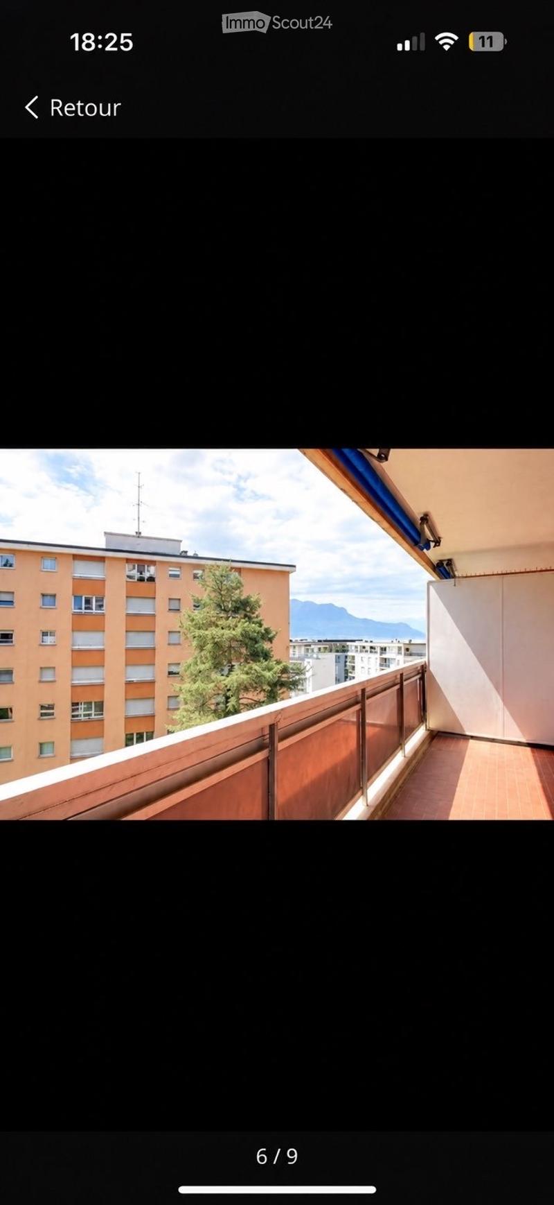 Balcony with wooden flooring, metal railing, and a view of a tree, building, and mountains.