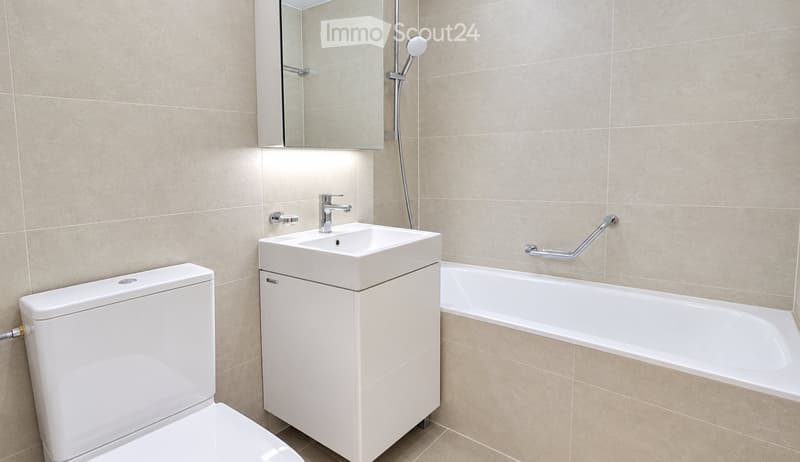 Modern bathroom with beige tiled walls, a white toilet, a sink with a modern faucet, a bathtub, and a large mirror above the sink.