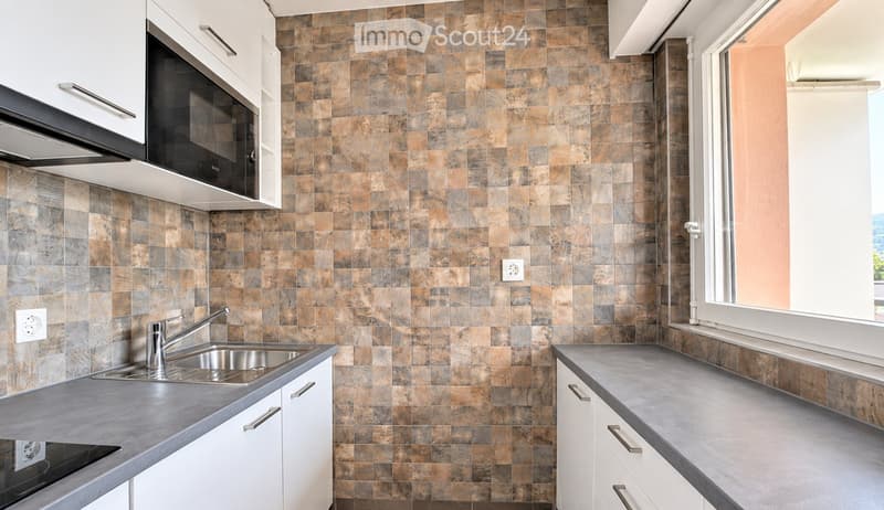Modern kitchen with white cabinets, stainless steel sink, microwave, and tiled backsplash.