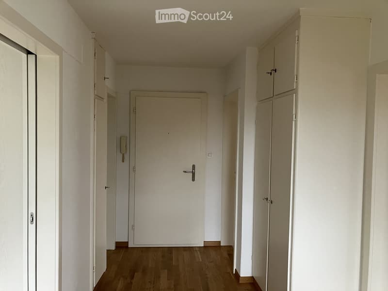 Empty hallway with wooden flooring, white walls, and multiple doors leading to other rooms.
