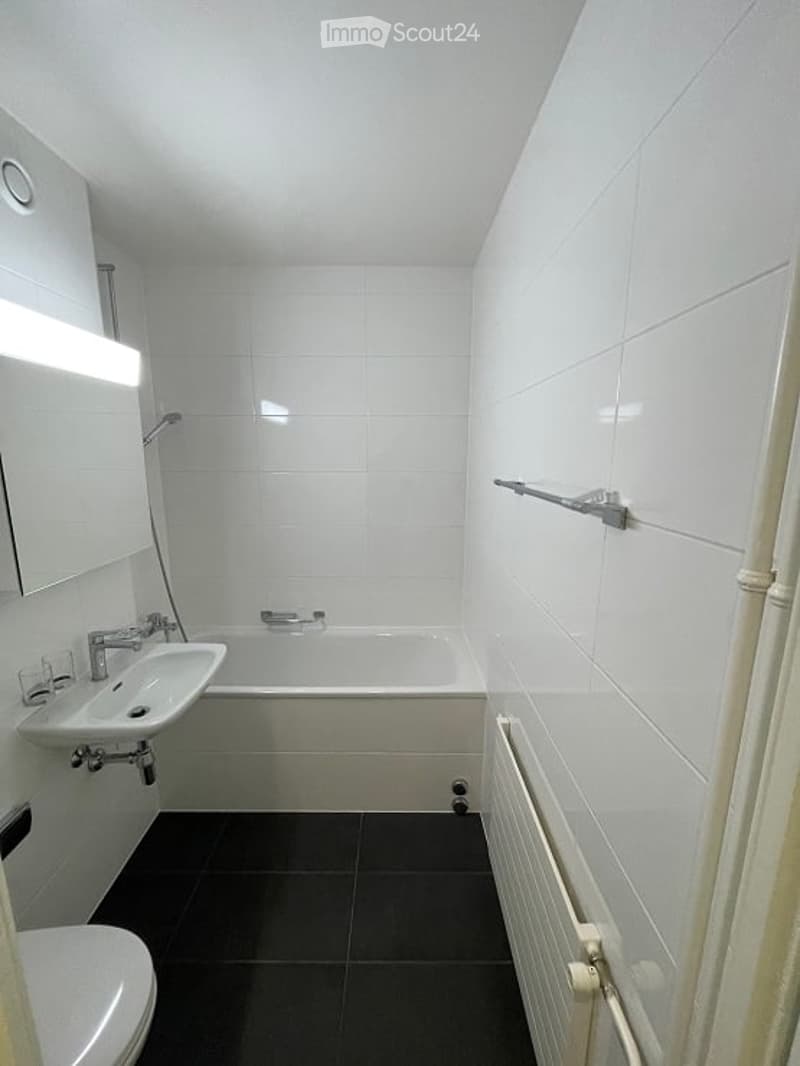 Modern bathroom with white tiles, black floor, sink, bathtub, toilet, mirror, and radiator.