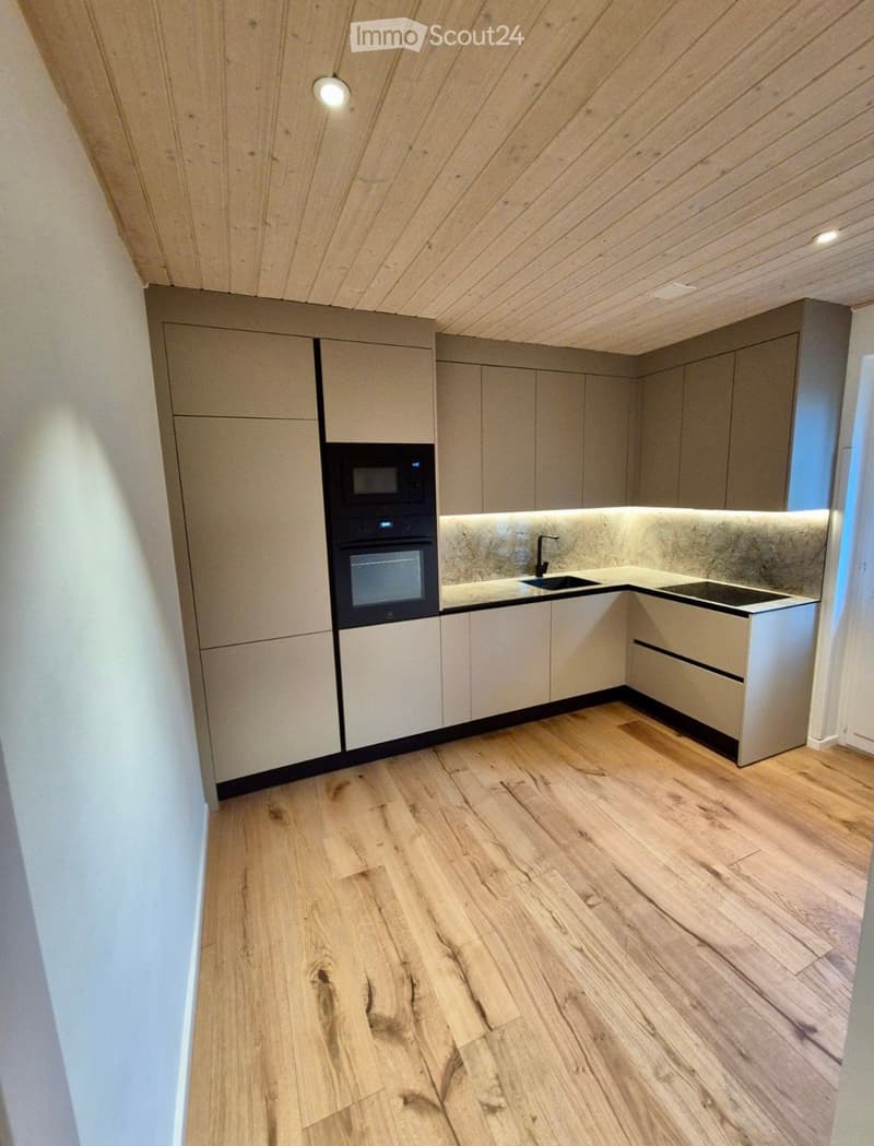 Modern kitchen with light wood cabinets, a sleek countertop, and built-in appliances including a microwave and oven. The floor is made of light wood planks.