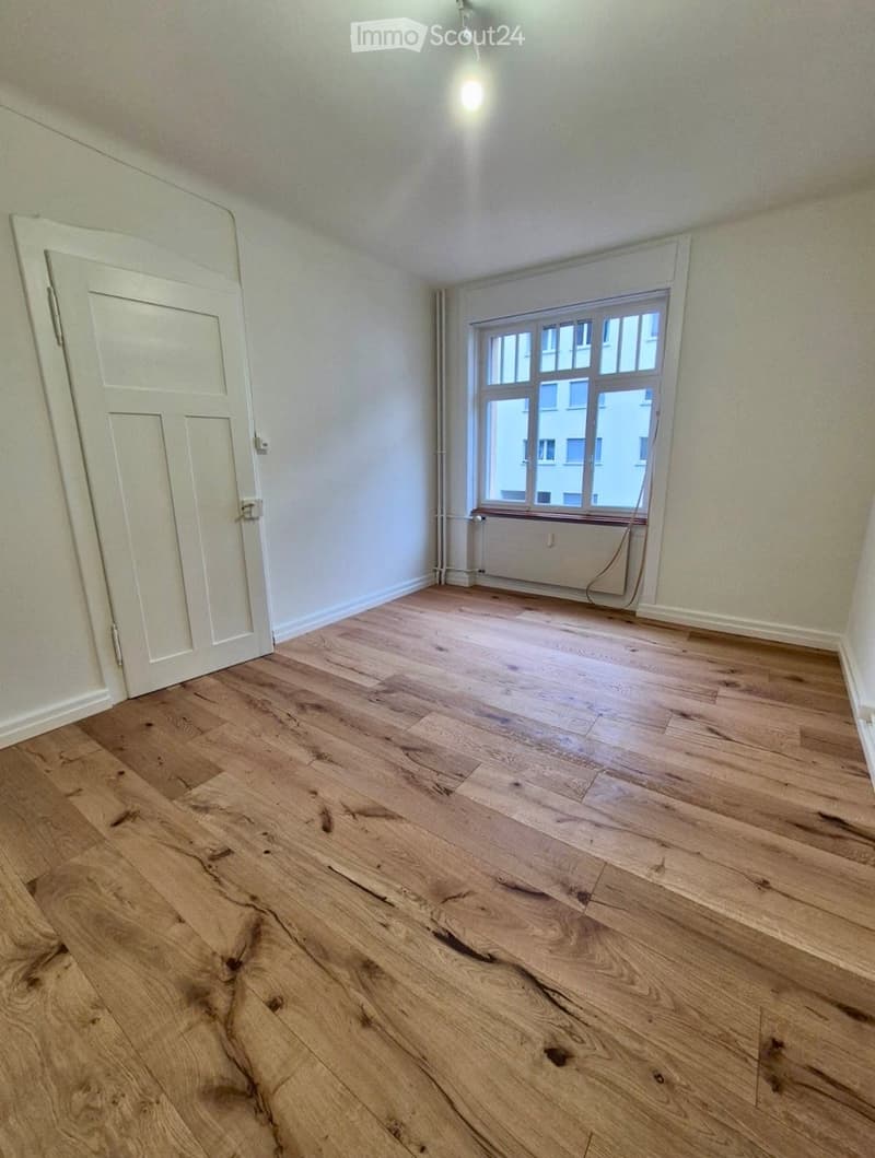 Empty room with wooden flooring, white walls, a single window, and a white door.