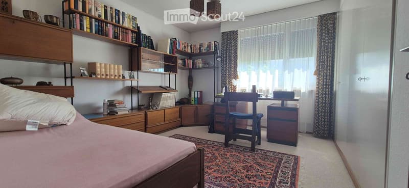 Cozy bedroom with a wooden bed, a desk with a chair, built-in bookshelves, and a patterned rug on the floor.
