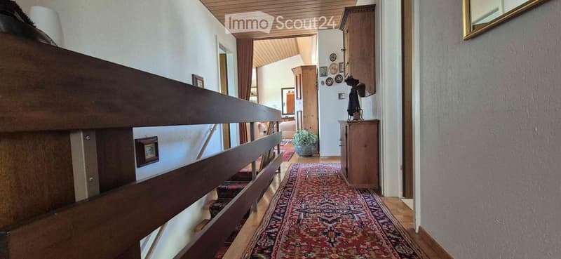 Staircase with wooden railing, patterned runner, and framed artwork on walls. Open view to adjacent room with furniture and decor.
