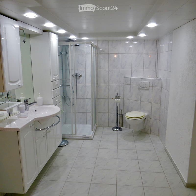 white tiled floor, white tiled walls, glass shower enclosure, white sink, white toilet, white cabinets, mirror