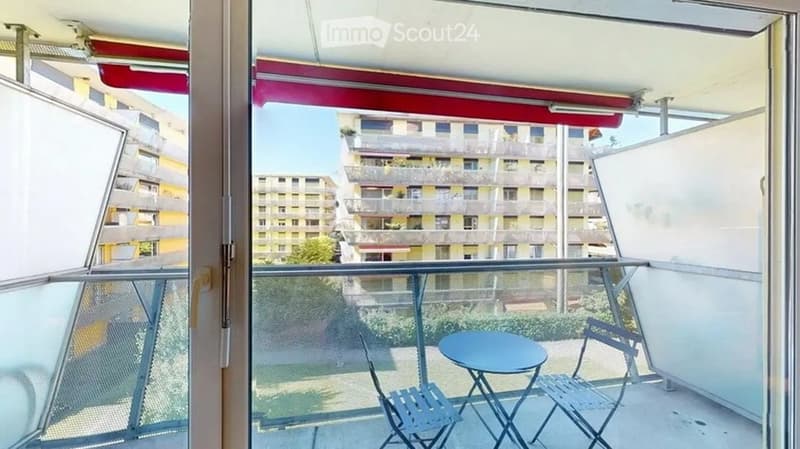 Balcony with a small round table and two chairs, overlooking a residential area with multiple apartment buildings.