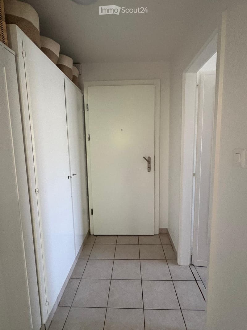 Empty hallway with tiled floor, white walls, and a closed door at the end.