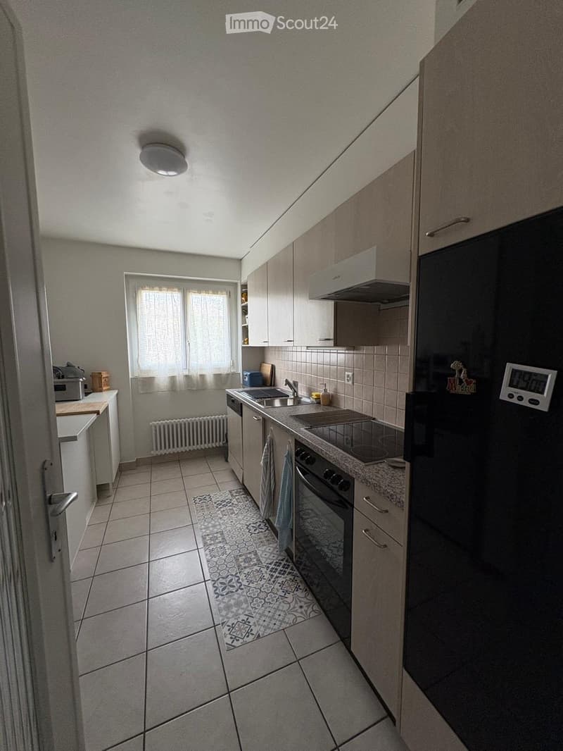 Modern kitchen with light-colored cabinets, a stainless steel sink, an oven, and a refrigerator. The floor is tiled, and there is a decorative rug in the center.