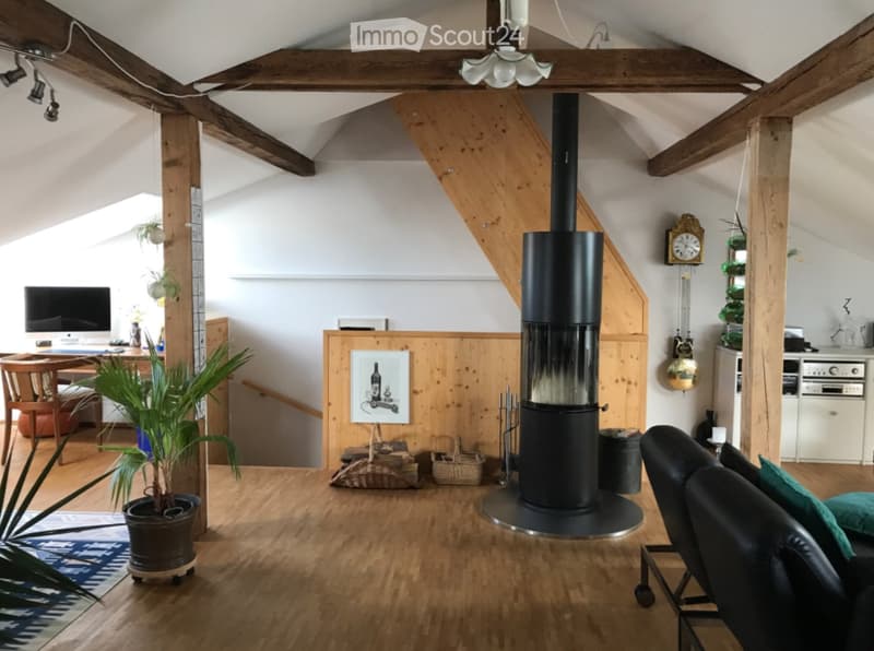 Cozy attic living space with wooden beams, exposed wooden floor, fireplace, sofa, table, chair, screen, and decorative plant.