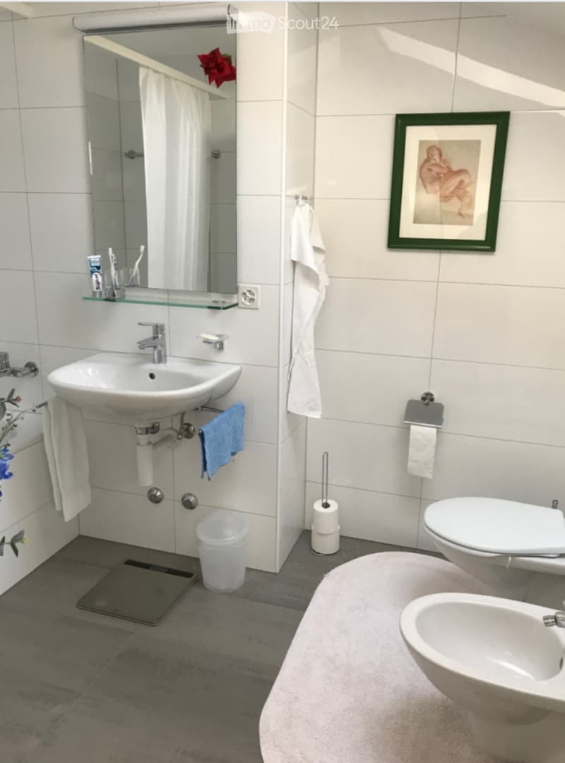 Modern bathroom with white tiles, a sink, mirror, toilet, bidet, bathtub, and various toiletries.