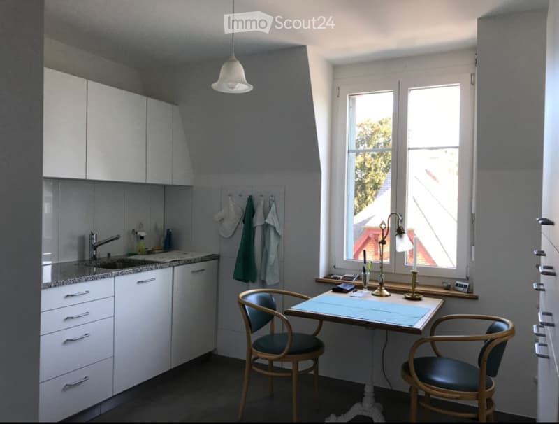 A modern kitchen with white cabinets, a sink, a small table with two chairs, and a window overlooking a view.
