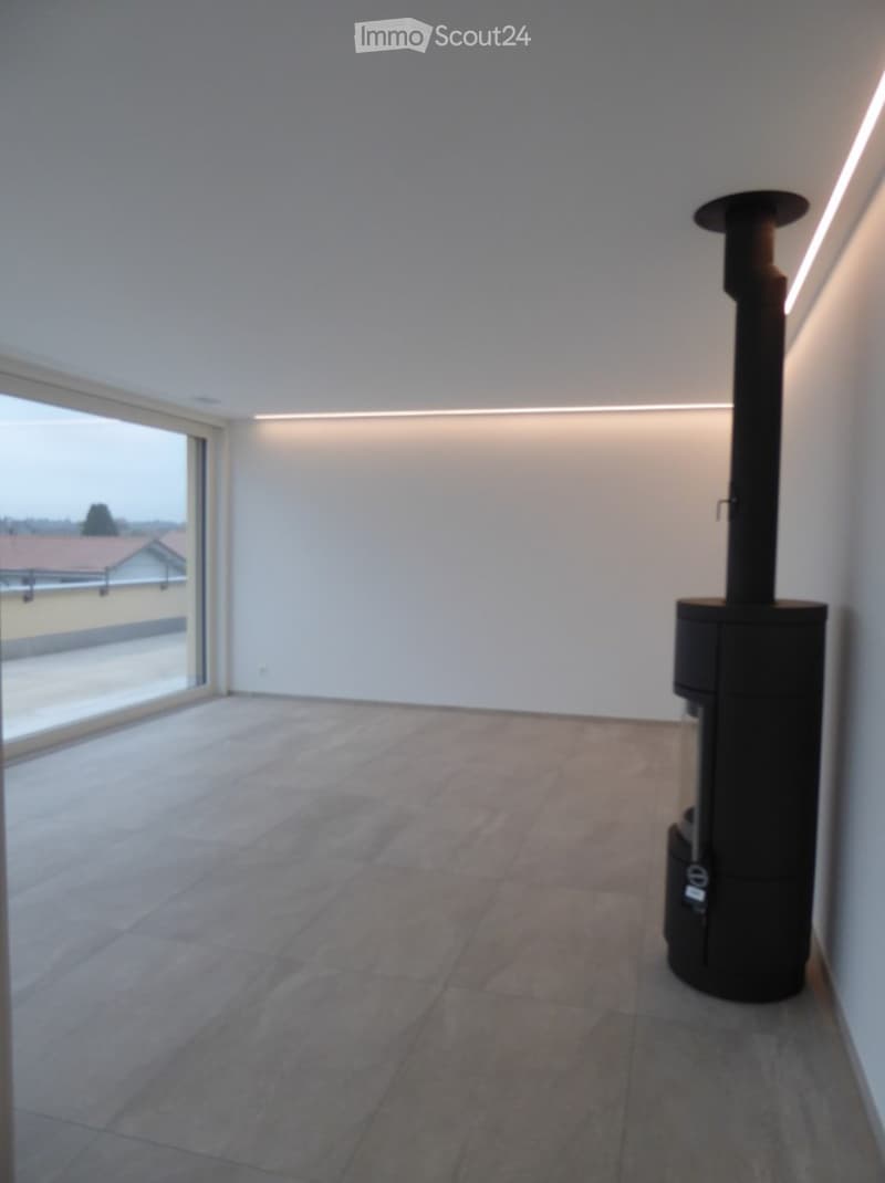 Empty room with tiled floor, white walls, large window, and a black wood-burning stove.