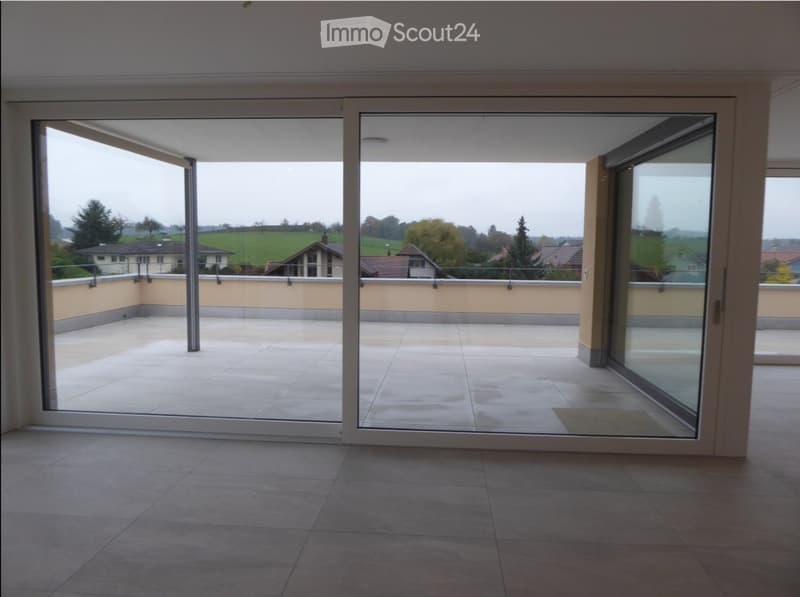 Empty room with tiled floor and large sliding glass doors opening to a tiled balcony with a view of the countryside.
