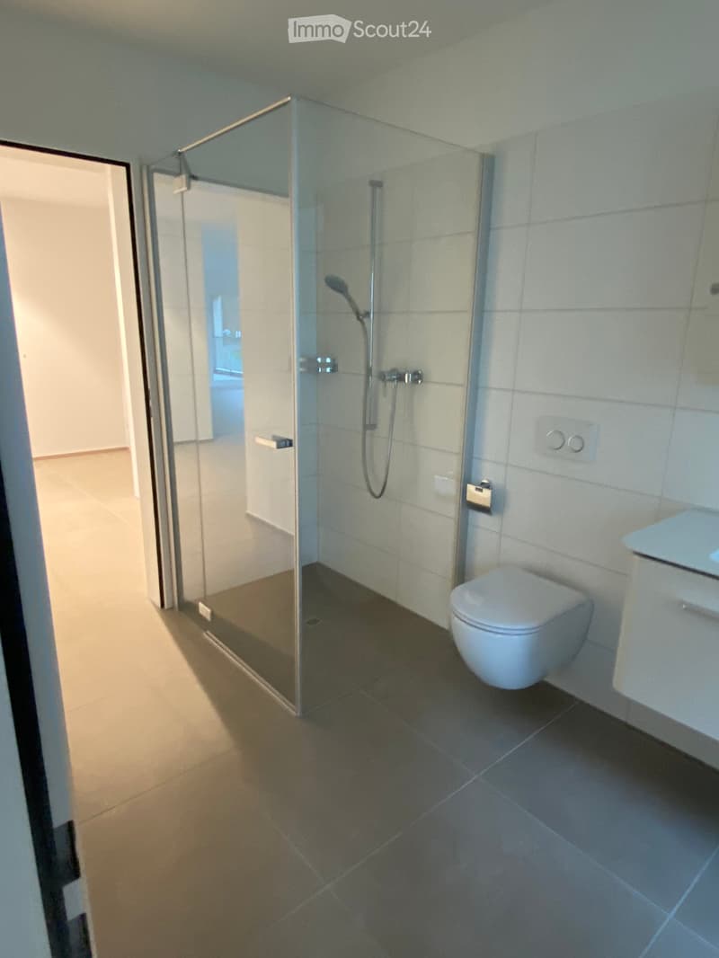 Modern bathroom with a glass-enclosed shower, toilet, and sleek tile flooring.