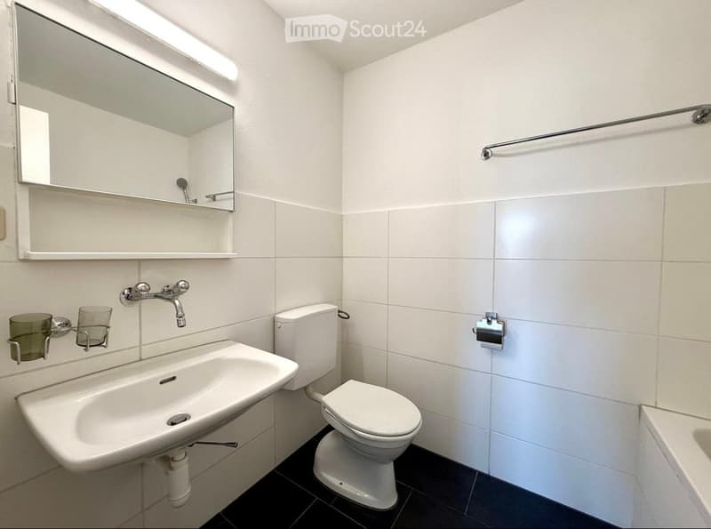 Modern bathroom with white tiles, a sink, toilet, mirror, and towel rack.