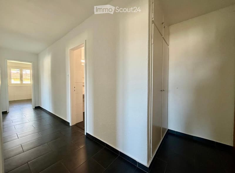 Empty hallway with dark tiled floor and white walls, featuring two open doors leading to adjacent rooms.