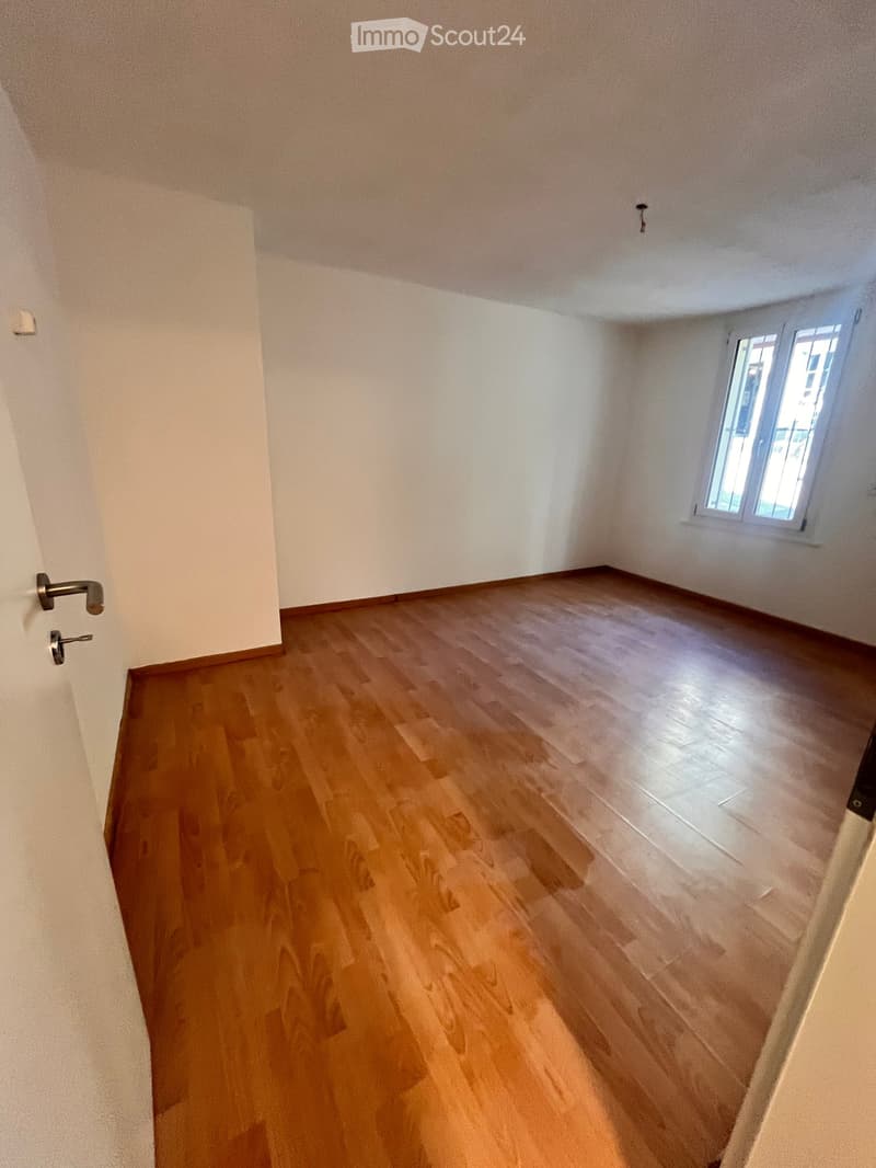 Empty room with wooden flooring and white walls, featuring a window and a door with a handle.