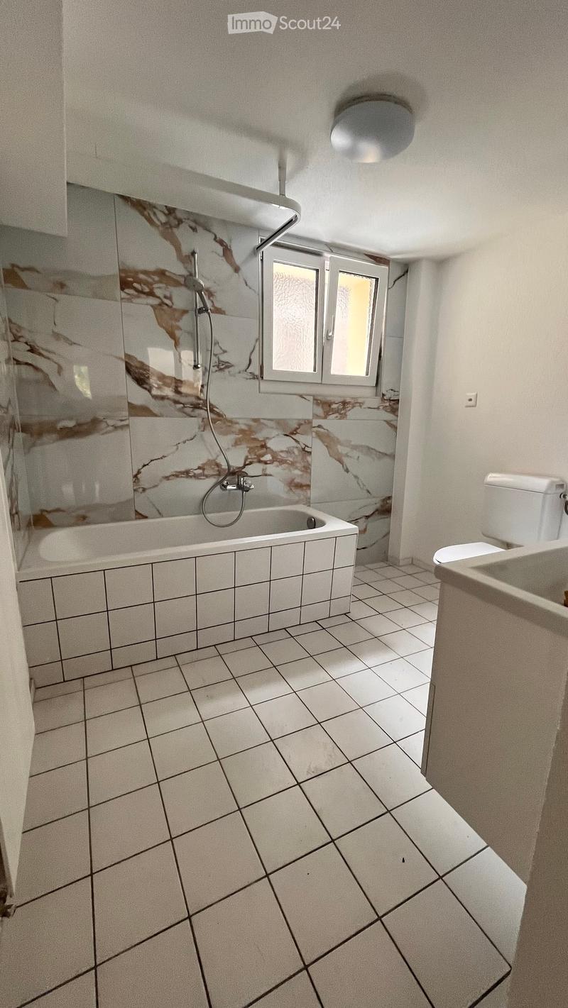 Bathroom with white tiled floor, marble-patterned shower walls, bathtub, toilet, and sink.