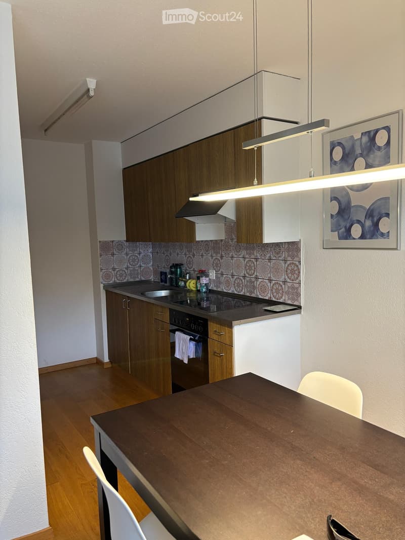 Modern kitchen with wooden cabinets, stainless steel appliances, and a dark wooden dining table with white chairs.