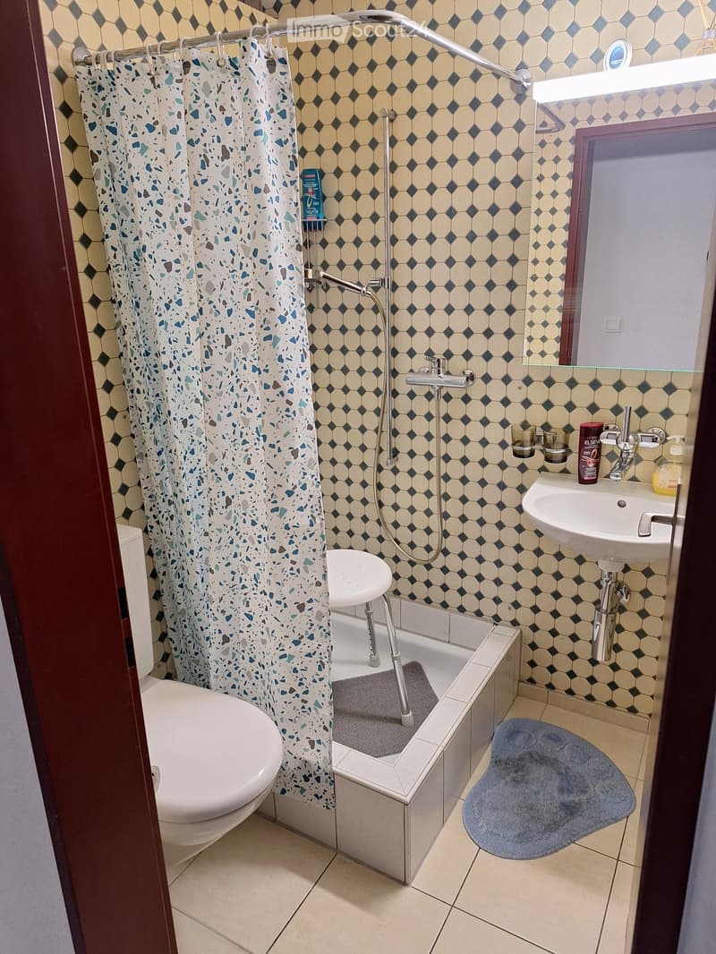 Bathroom with hexagonal tiles, toilet, bathtub with shower curtain, sink, and bath mat.