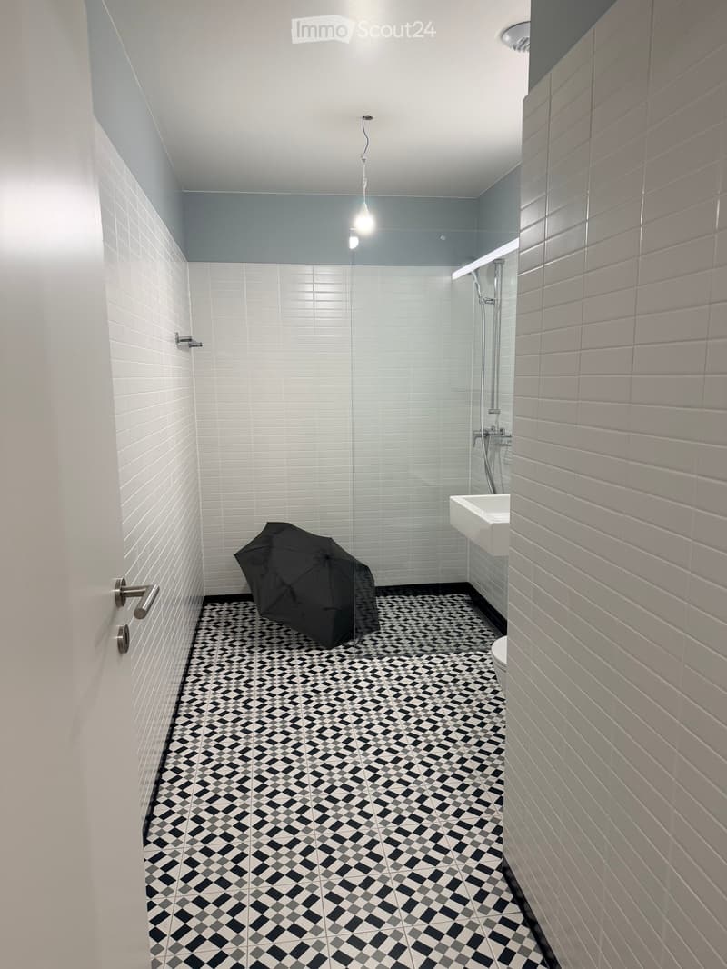 Modern bathroom with white tiled walls, black and white checkered floor, glass shower enclosure, and a single sink.