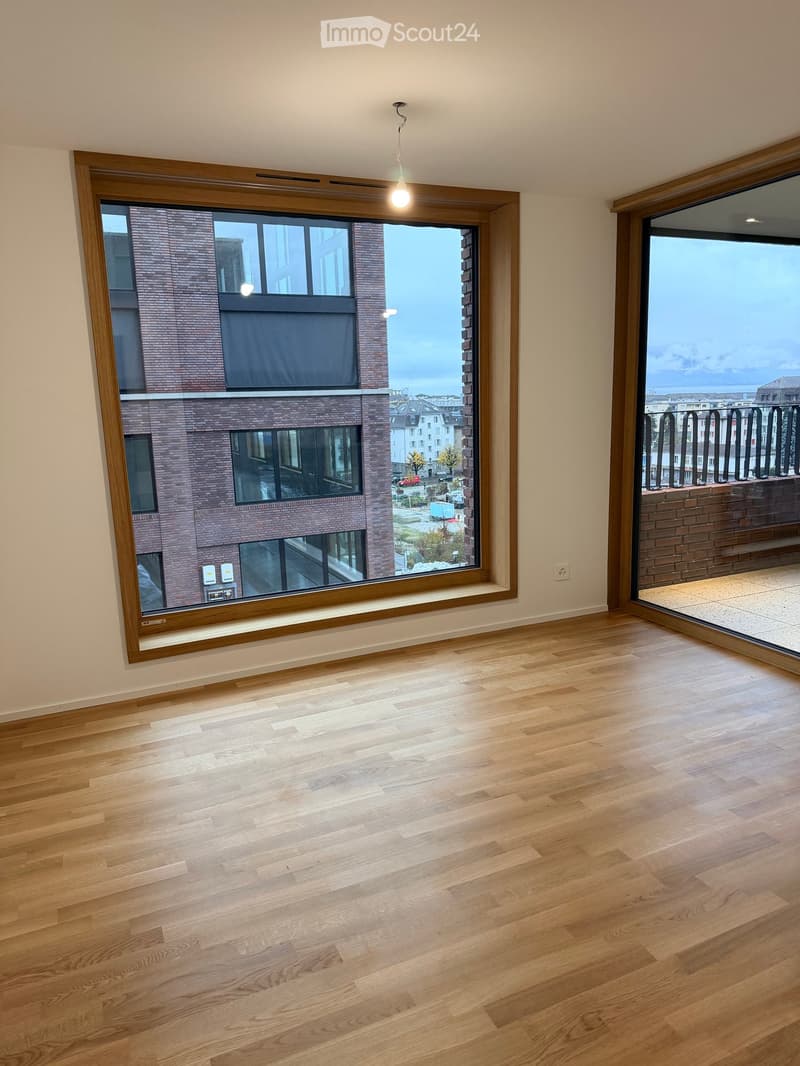 Empty room with wooden flooring, large windows, and a sliding glass door leading to a balcony.